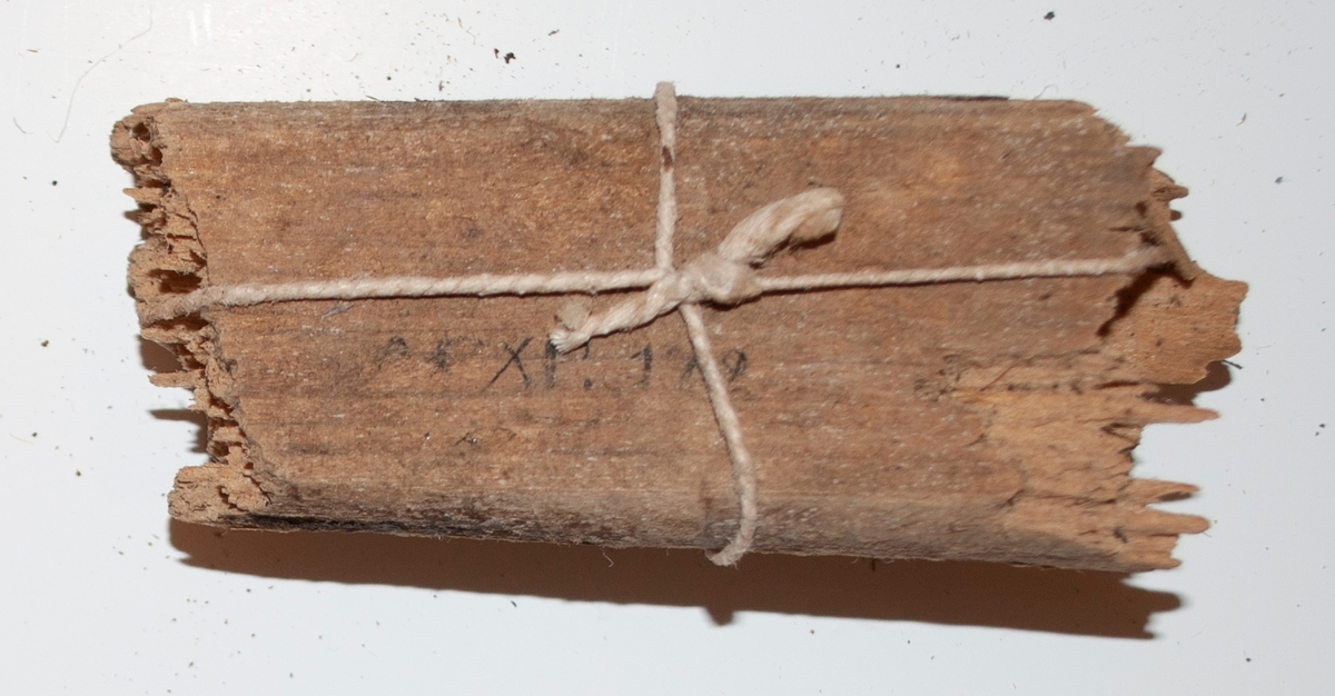 Två träfragment av båten. Det ena fragmentet är rektangulärt och det är knutet ett snöre om den.