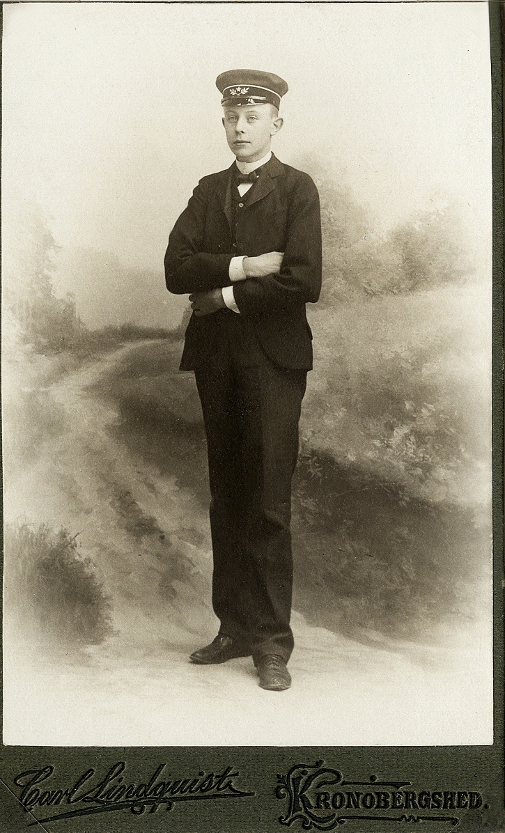 En ung man i mörk kostym med väst, skolmössa m.m.
Helfigur, halvprofil. Ateljéfoto 1907.