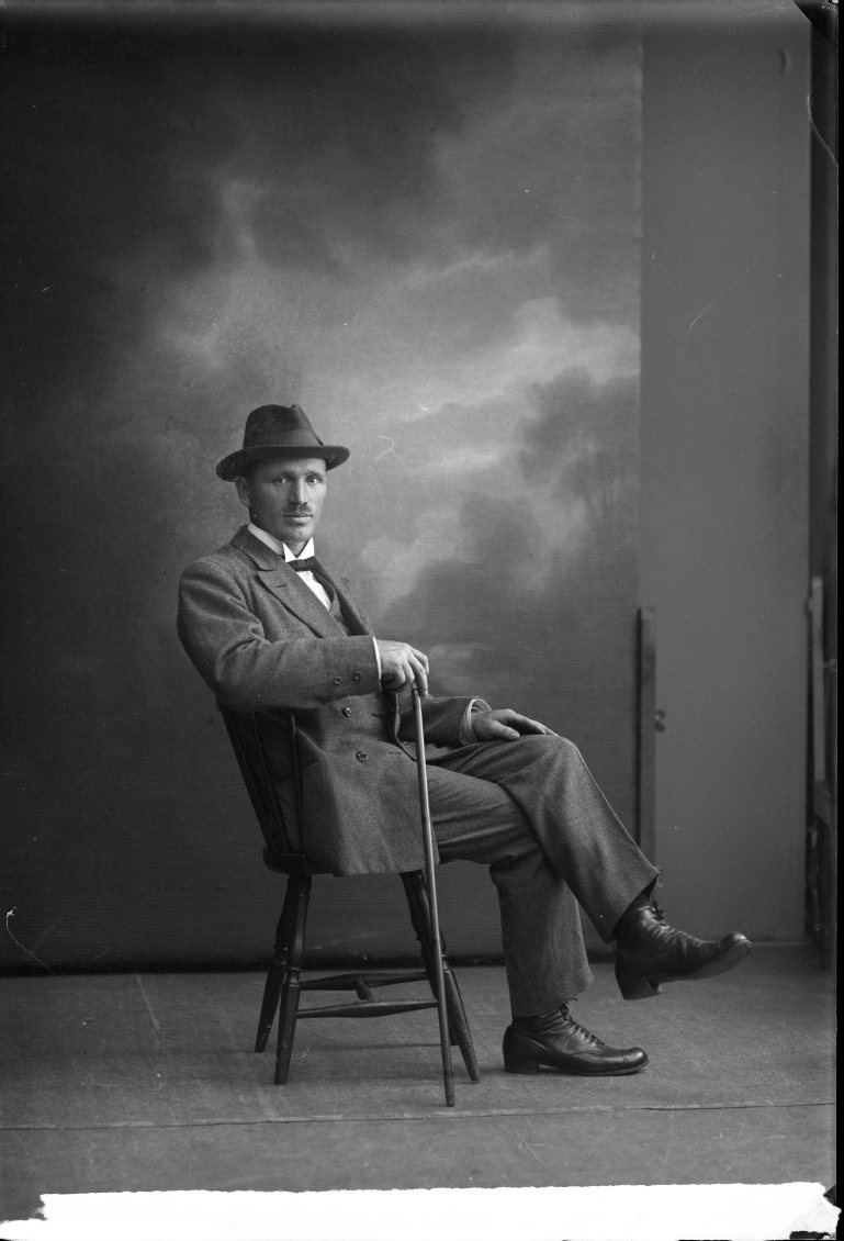 En man med hatt och spatserkäpp sitter på en stol.
