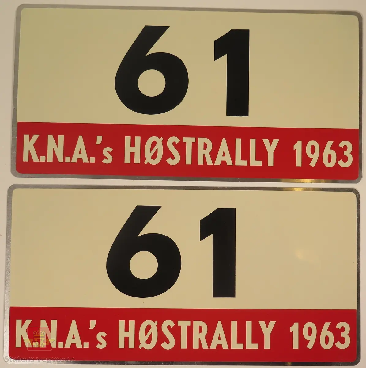 Hovedsakelig hvite metallskilt med et mindre rødt markeringsområde. Grupperingen med skilt har også nummeret "61" påført seg, dette er en indikasjon på deltakernummer.
Påskrift: K.N.A.'s HØSTRALLY 1963