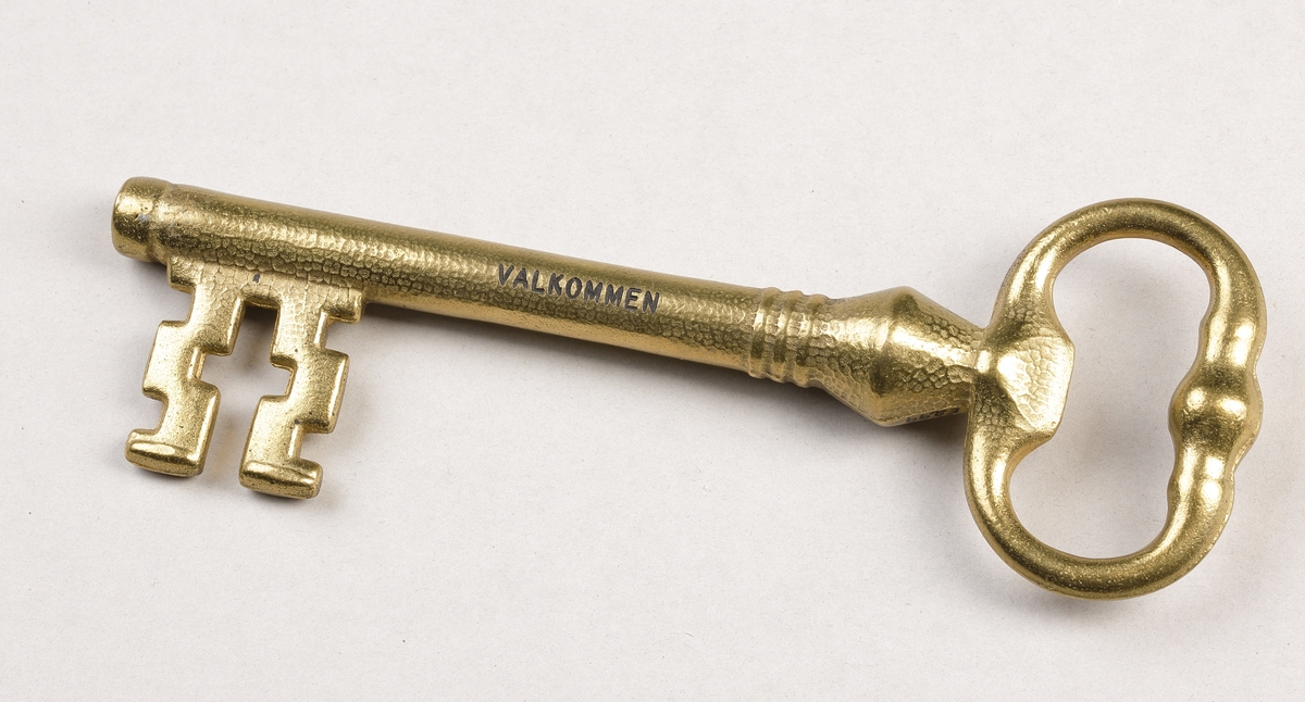 Nyckel i gjuten mässing med ax liknande ett kors. På ena sidan av nyckeln finns texten "VALKOMMEN" och på andra texten "CITY OF LINDSTROM". De präglade texterna är fyllda med svart färg.