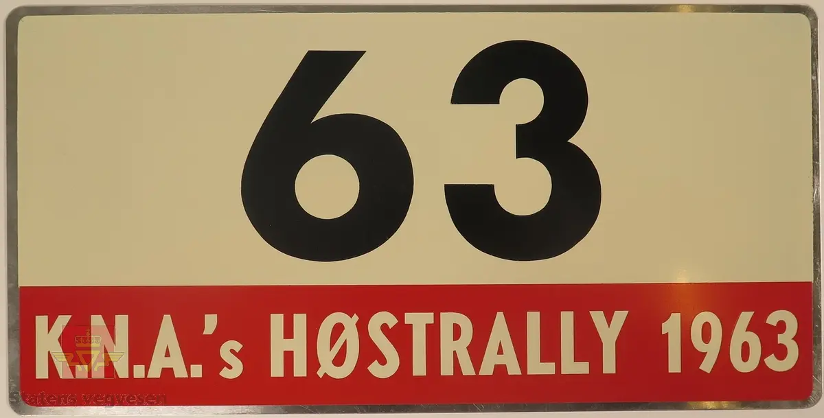 Hovedsakelig hvitt metallskilt med et mindre rødt markeringsområde. Skiltet har også nummeret "63" påført seg, dette er en indikasjon på deltakernummer.
Påskrift: K.N.A.'s HØSTRALLY 1963