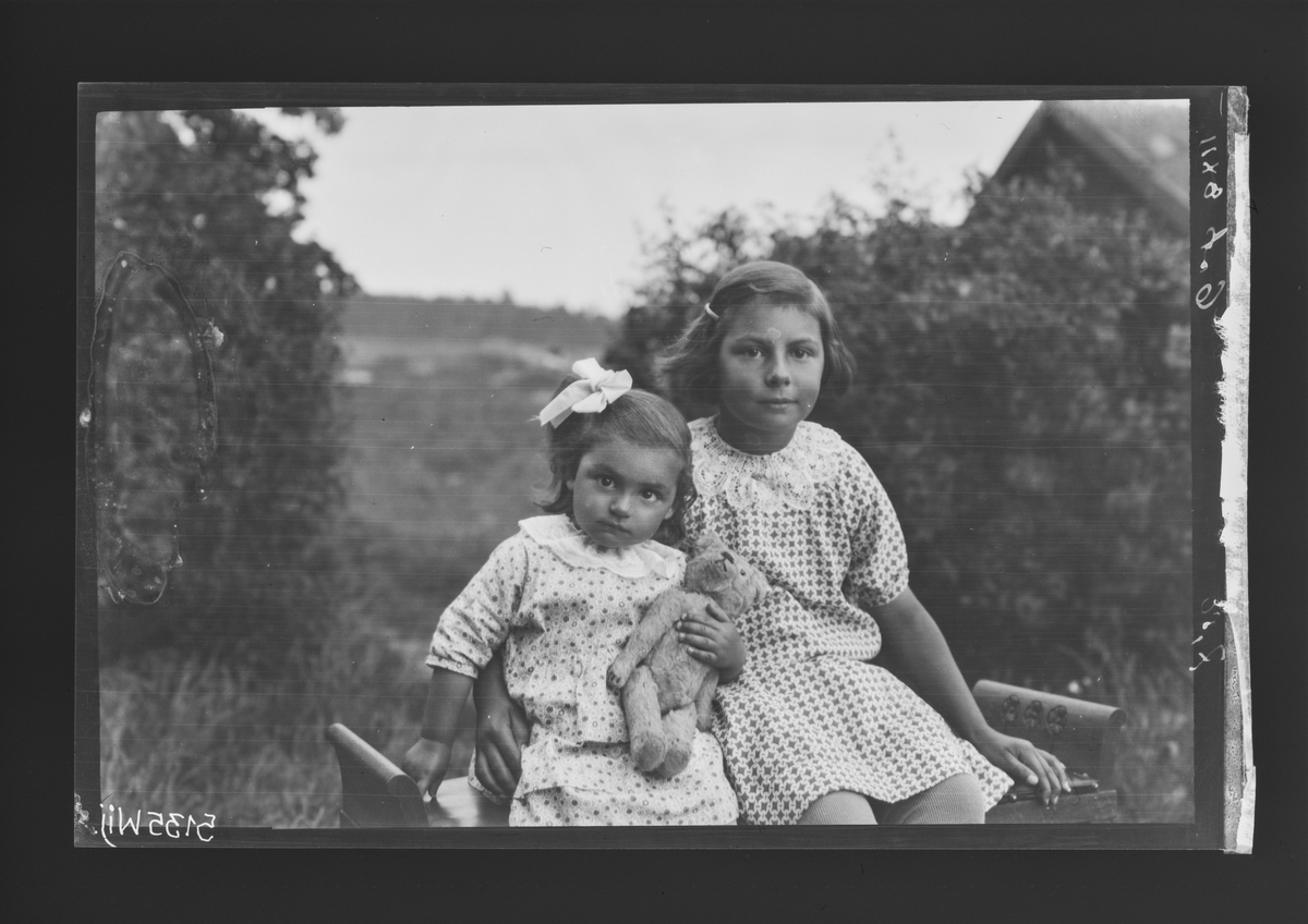 Fotografering beställd av Fagerlind. Föreställer sannolikt jordbruksarbetaren Johan Axel Fagerlind och hans hustru Signe Axelina Solmans två döttrar Anna Maria (1922-2011), och Mary Elisabeth (1928-) som i famnen håller en teddybjörn.