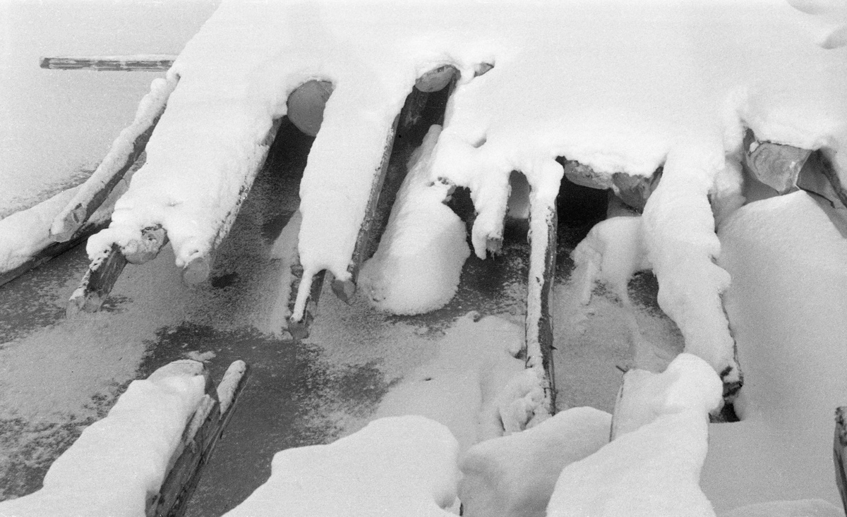 Nediset og delvis nedsnødd tømmer på Glomma på Tynset i Hedmark, vinteren 1952. Ved å legge tømmeret på isen på denne måten sparte man seg for utislagsarbeidet som måtte til, om fløtingsvirket hadde ligget på elvebakken. Dessuten lå stokkene lett tilgjengelig for måling og merking. Det var imidlertid flere betenkeligheter knyttet til å plassere tømmeret på isen på denne måten. Når elva gikk opp her, ville tømmerstokkene følge med nedover, men det kunne få hard medfart dersom isflakene pakket seg sammen og dannet propp lengre nede i vassdraget. Vel så problematisk var det at det tømmeret som ble lagt på elveisen, i hvert fall det som lå underst, lett ble eksponert for kjøving, noe som innebar at det ble vannmettet og tungt, og følgelig lett kunne synke på den lange fløtingsstrekningen sørover mot industrien ved den nedre delen av vassdraget.