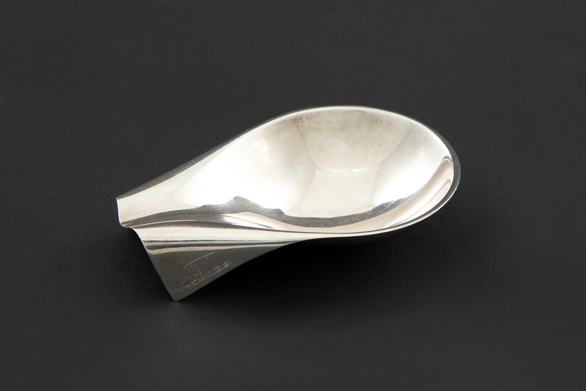 Pipestativ i sølv. Dråpeformet skål som smalner sammen til en forlenget endeparti med to nedbrettede kantfolder med monogram.
