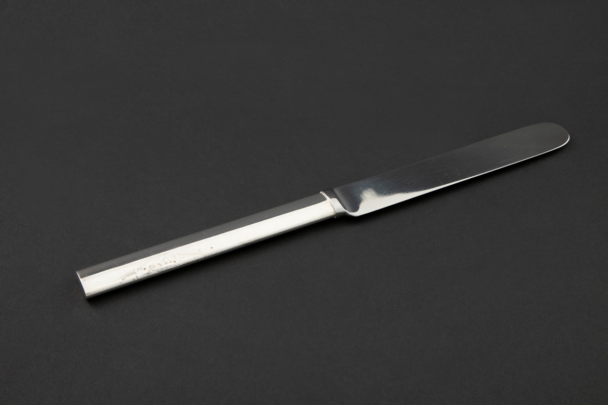 Stor kniv i sølvplett. Ovalt skaft med rett avslutning og bredere knivblad. Fra bladets halvrunde avslutning er egg og rygg parallelt.
