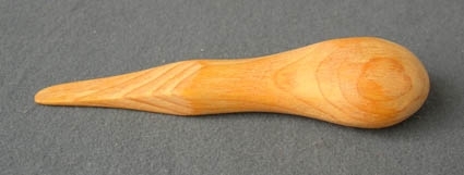 En s.k. petpinne eller påpetare som används vid flätning av näver. Den är tillverkad av furu med plan undersida och ett runt skaft som smalnar av och tunnas ut mot en rakt avtagen spets. Märkt med LK inne i varann likt ett bomärke.