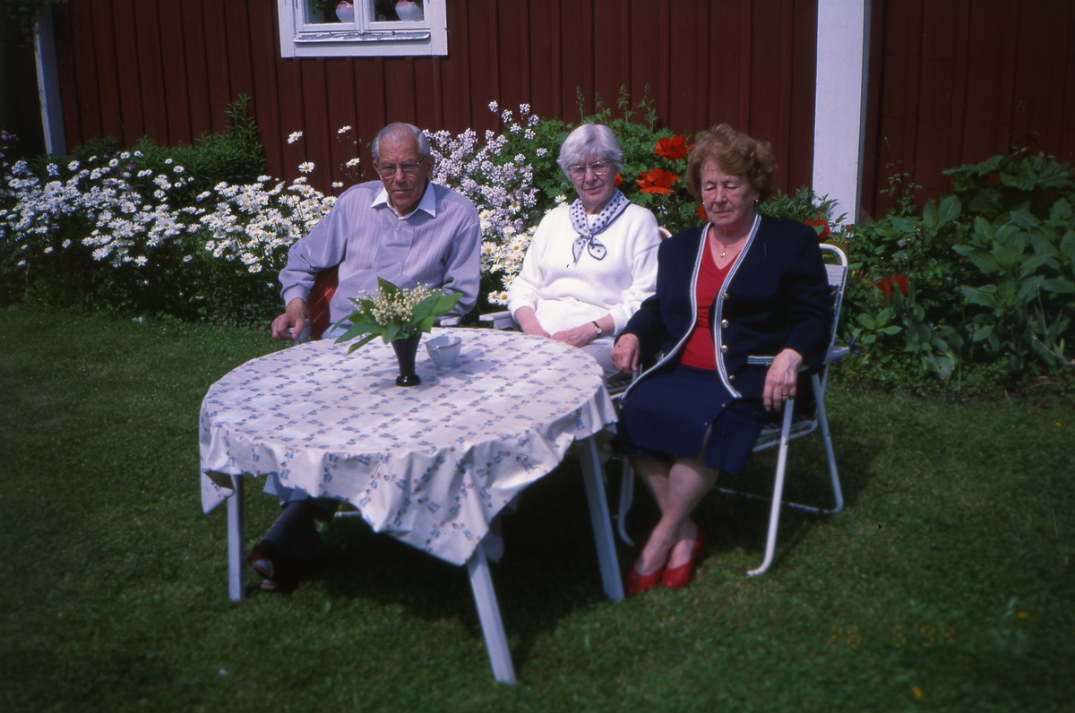 Adéle(till höger i bild) och en man och kvinna sitter vid ett bord i trädgården hemma på gården Sunnanåker 26 juni 1994.