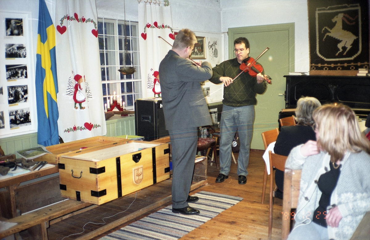 Fiolspel vid öppningen av Bollnäs-kistan, juldagen 1999. Åhörare sitter vid bord intill och lyssnar.