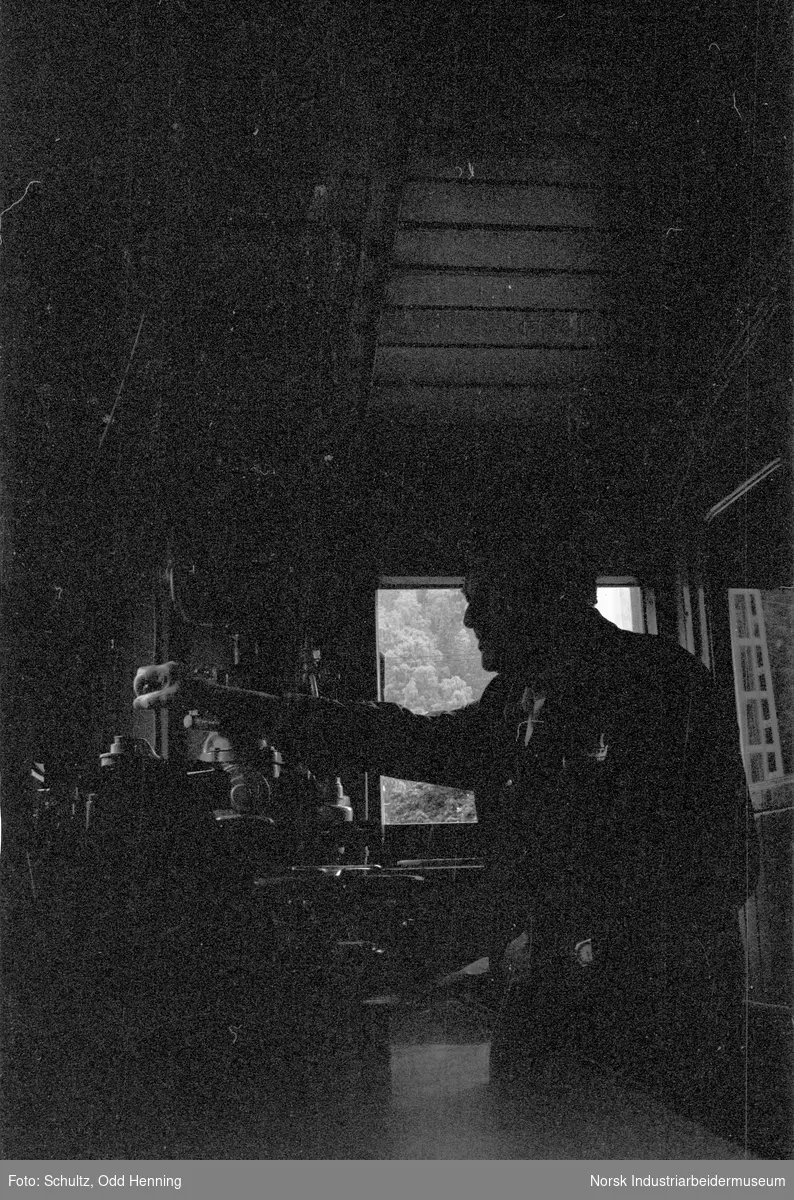 Mann inne i lokomotiv, med instrumenter og apparatur til styring og kontroll.