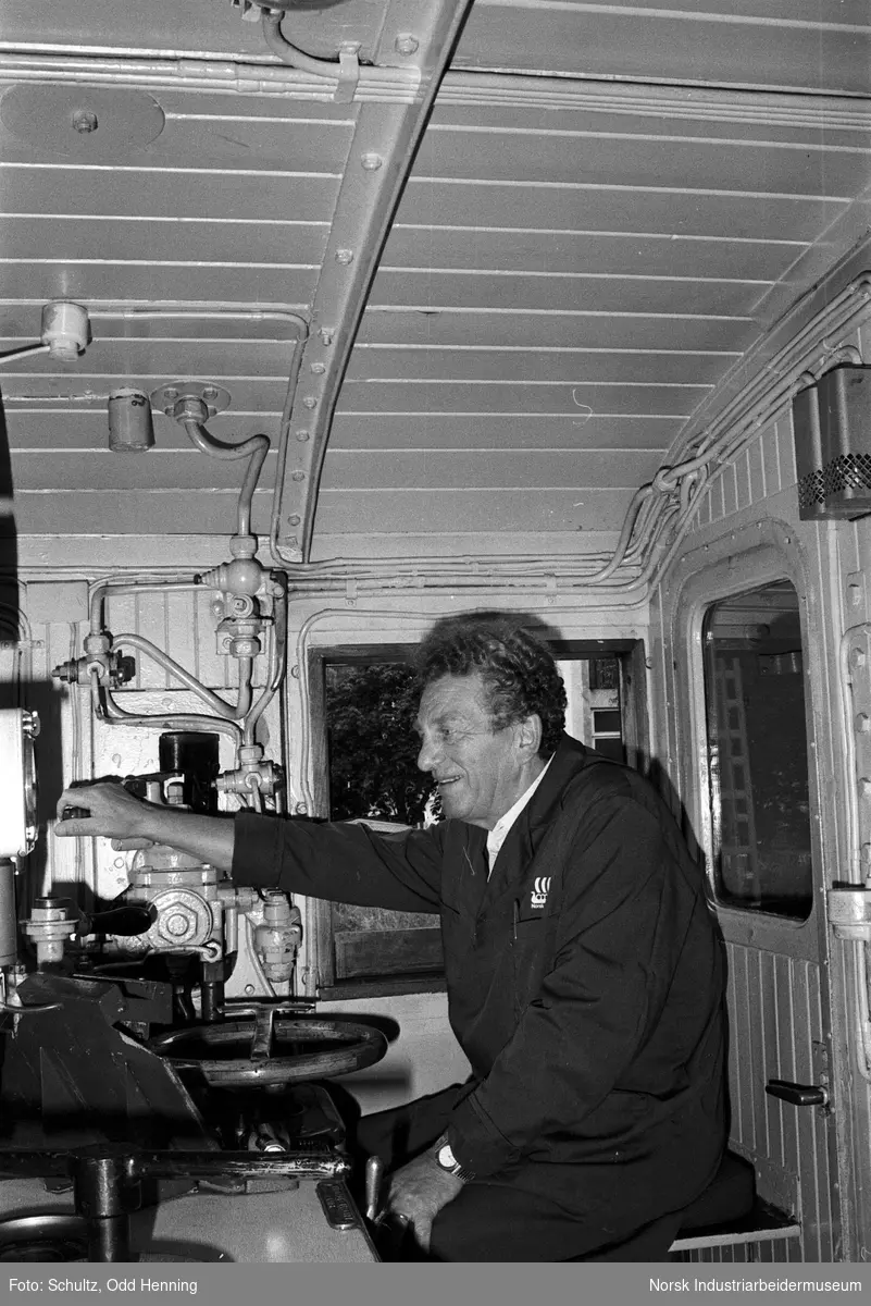 Mann inne i lokomotiv, med instrumenter og apparatur til styring og kontroll.