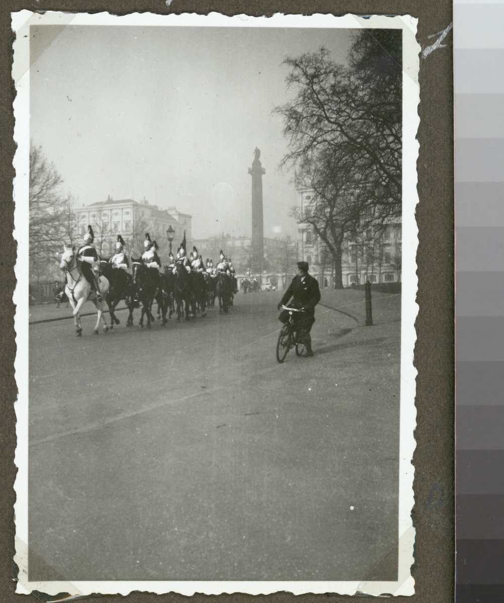 Bilden visar engelska soldater i paraduniformer till häst som rider på Horse Guards road i London. I bakgrunden syns monumentet "Duke of York Column"