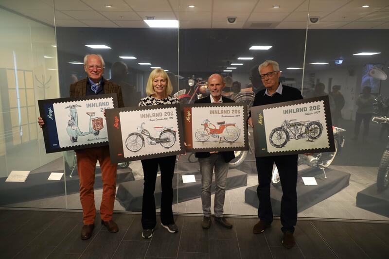Fire personer holder pappskiver med bilde av frimerker med norsk mopeder, motorsykler og scooter.