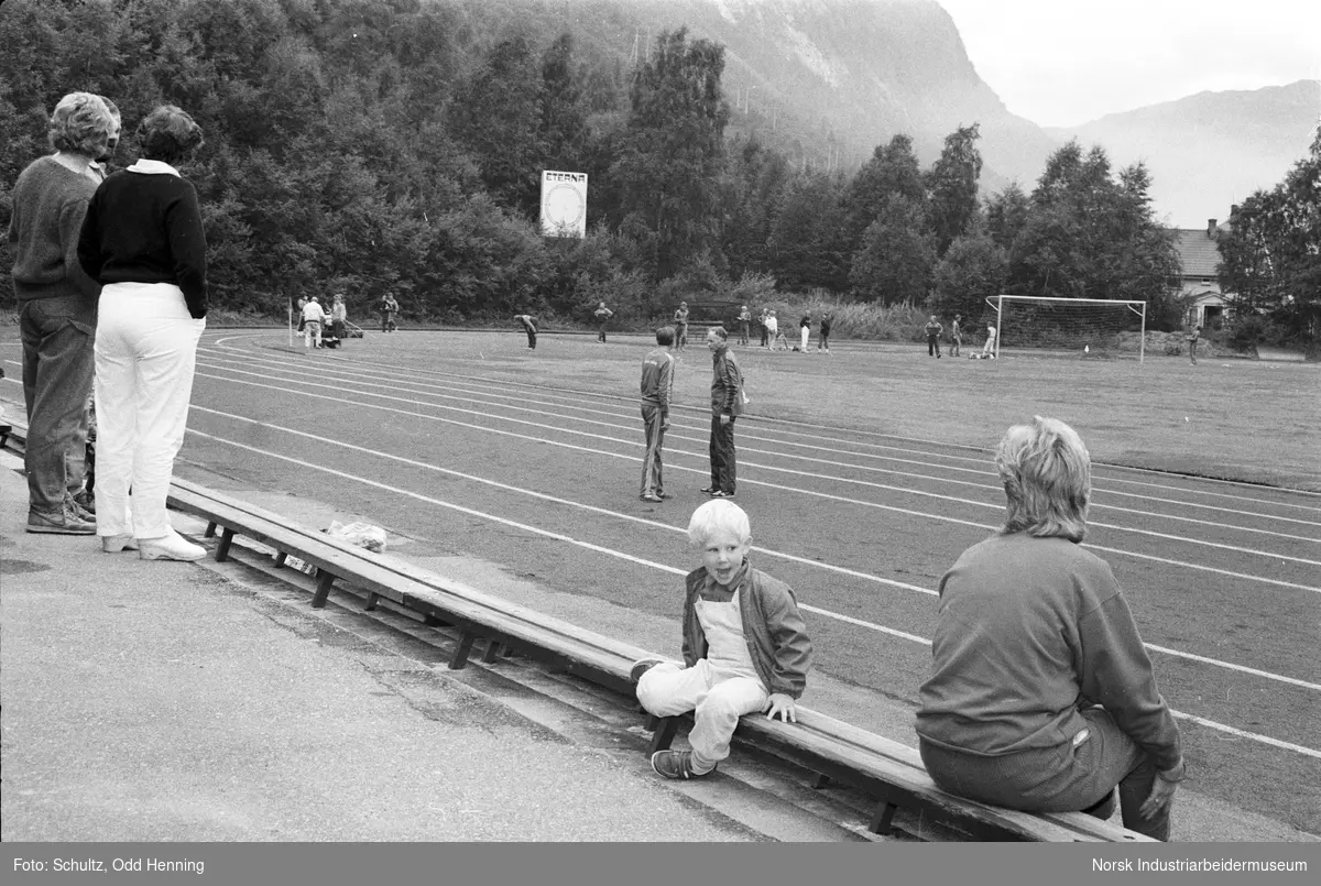Mennesker på Rjukan stadion, under Hydromesterskap i friidrett. En gutt sitter på kanten av løpebanen.