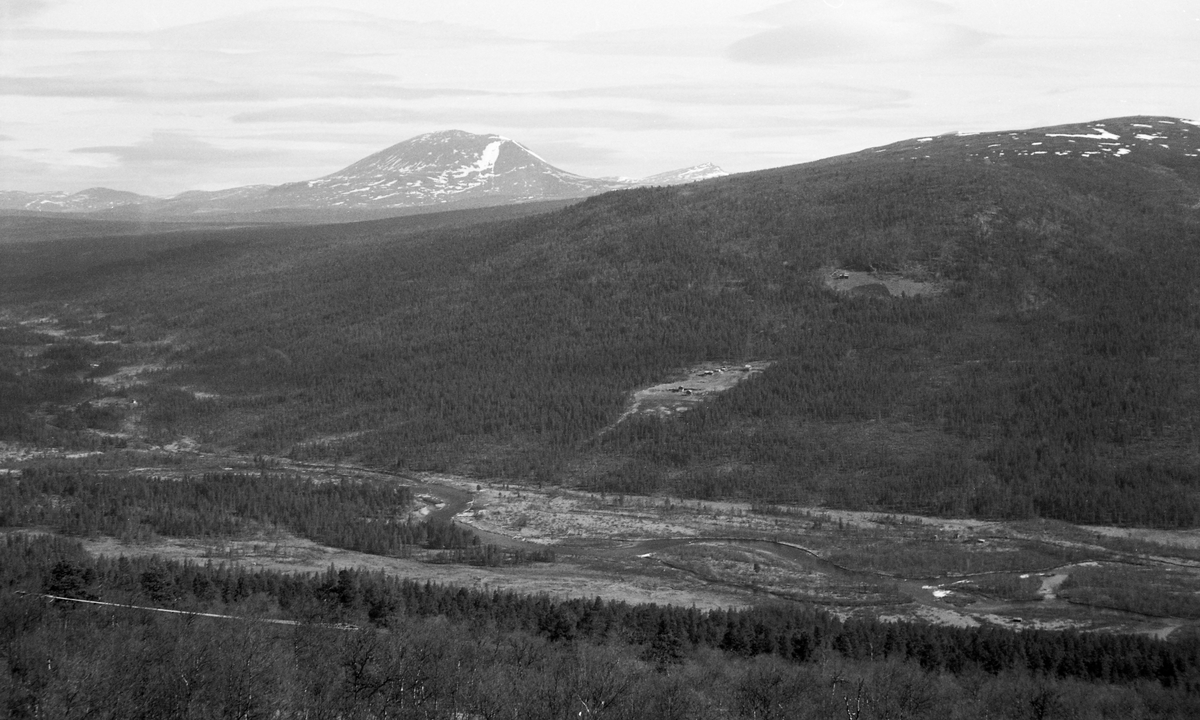 Landskapsbilde fra Skåbu i Nord-Fron i Gudbrandsdalen. Fotografiet er tatt på tvers av dalføret der den nedre delen av elva Hinøgla renner mot innsjøen Slangen. I den sørvestvendte lia på den andre sida av elva ser vi jordvegen på småbrukene Perslåa og Hovda som lysninger i et terreng der det ellers vokste fjellskog. Fjellet i bakgrunnen er Heidalsmuen (1745 m. o. h.), som ligger i nabokommunen Sel. Elveløpet i forgrunnen ligger cirka 670 meter over havet.