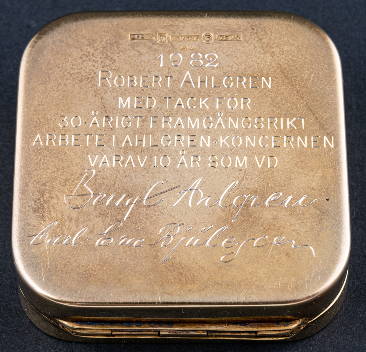 Tablettask av förgyllt silver med emalj med tillhörande rött etui i konstläder. Tablettasken har hämtat sitt utseende från den gröna Läkerolasken.