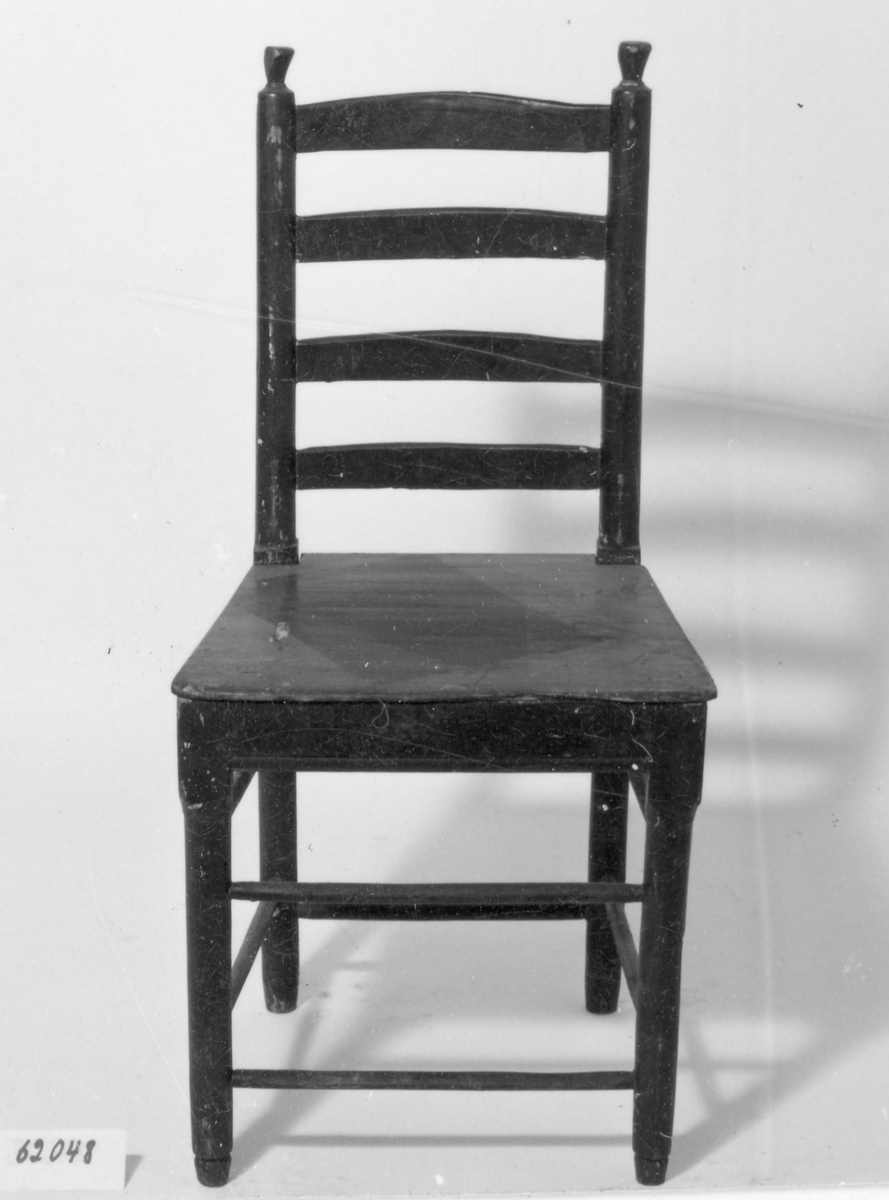 Brunmålad stol med 4 raka svarvade ben, dubbla svarvade tvärslåar mellan benen, träsits. Rygg med 4 tvärslåar mellan svarvade stolpar avslutas med svarvad knopp.