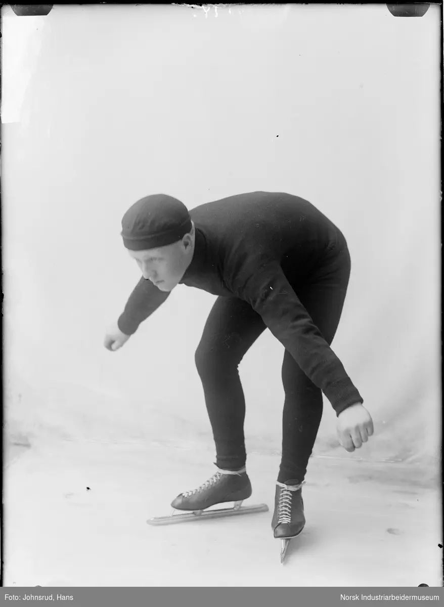 Portrett av mann med lue posert som en skøyteløper med skøyter på føttene.