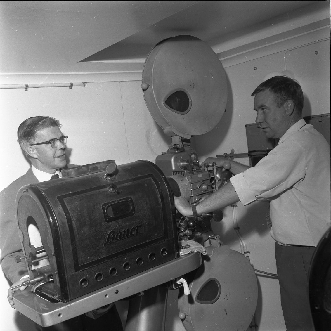 Två män står vid en filmprojektor som just installerats i Gränna biograf. Till vänster biografägaren B Palmér och till höger chefsinstallatören ingenjör E Schederin.