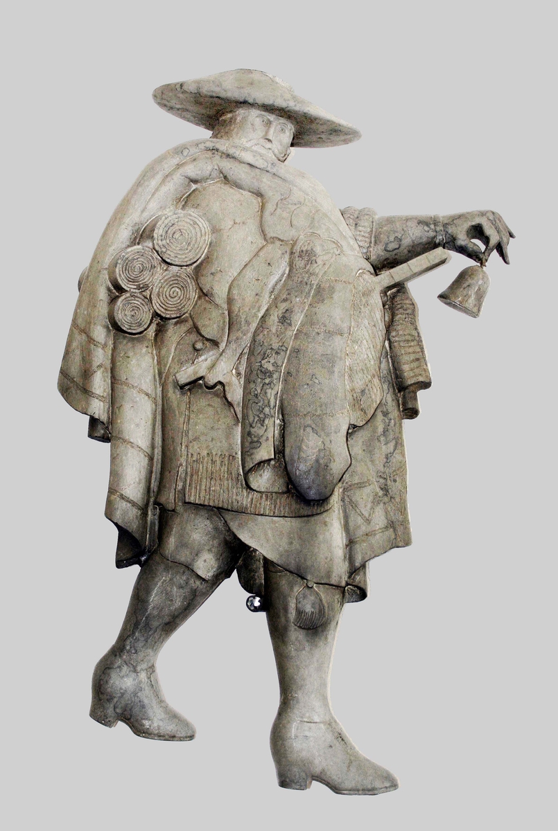 Väggskulptur i patinerad brons. Föreställer "Knallen". Gående, mustaschprydd man, i bredhättad hatt. På höger sida, bär han textilier och alnmått. I vänster hand, håller han en pingla. Proveniens Algot Johansson AB, Borås.

Funktion: Väggdekoration