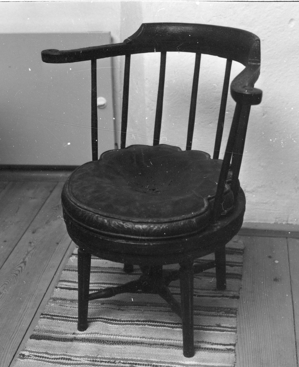 Svartmålad karmstol med rund sits, skinnklädd lös dyna. Halvcirkelformat ryggkrön, åtta rundsvarvade ryggpinnar, fyra kannelerade ben med svarvat kryss.