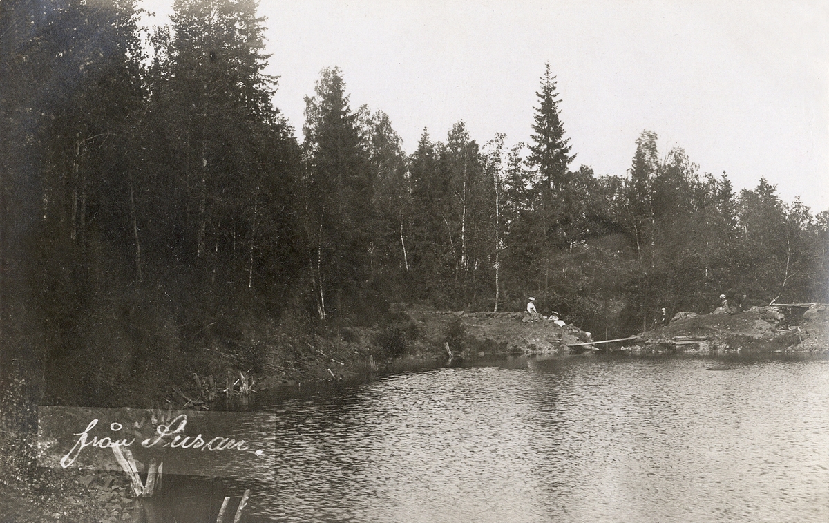 Några personer på utflykt sitter på några klippor vid en sjö. Ca 1905.