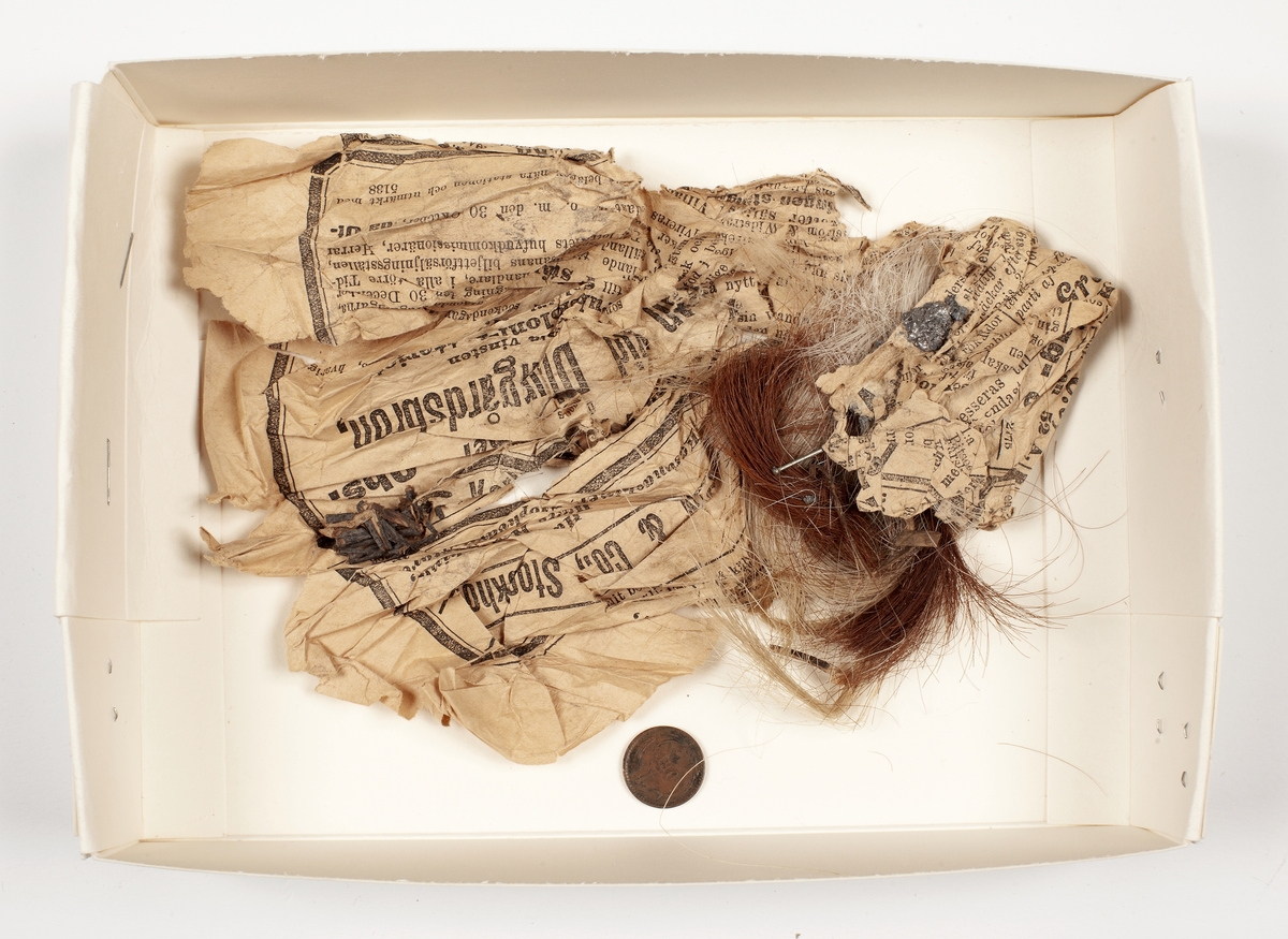 Trollknyte innehållande tussar av ljust och rött hår från nötkreatur, klumpar av bly, tre stålnålar, torkade växtdelar, en dansk 1-öring från 1887, allt insvept i ungefär en halv tidningssida.