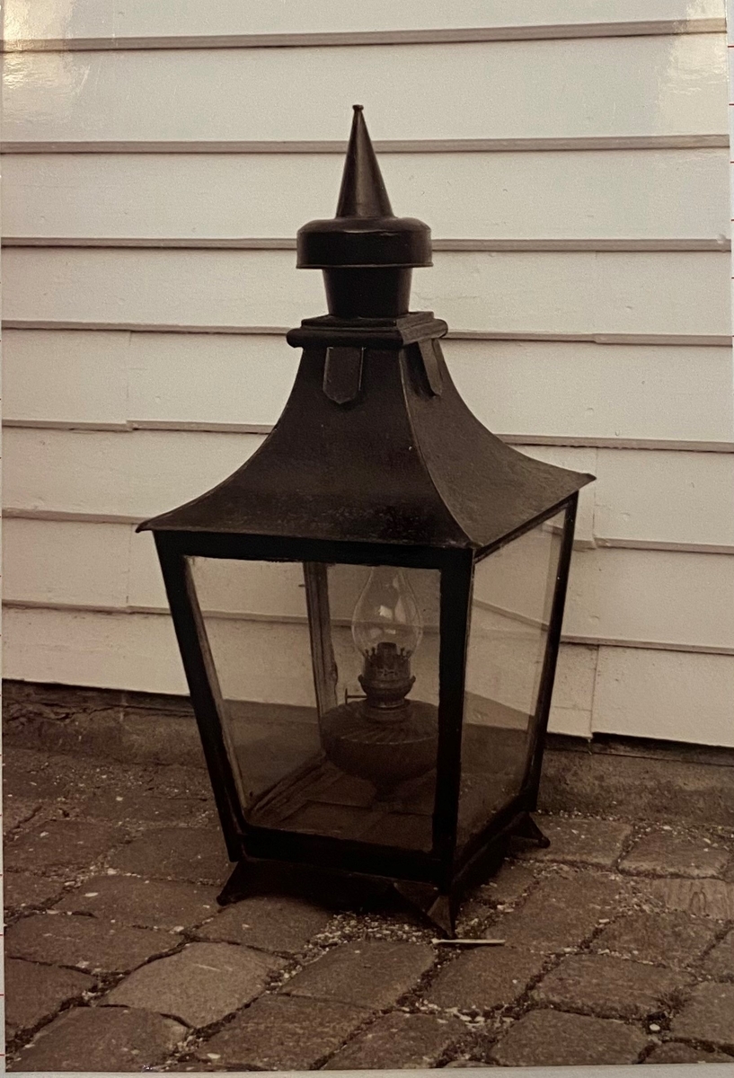 Parafinlampe, brukt som gatelykt i Mandal. Lykten har kvadratisk grunnform og rosa oljebeholder.
