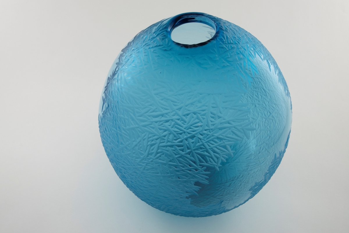 Asymmetrisk dråpeformet skulptur i blåfarget klart glass. Deler av overflaten er behandlet med sliping, sandblåsing og polering, slik at det oppstår en matt struktur av kryssende diagonale linjer som skaper assosiasjoner til rim/frost. Slik dannes det en virkningsfull kontrast til de ubehandlede partiene, som muliggjør at betrakteren kan studere dekoren fra både ut- og innsiden. Sirkulær åpning ved vasens topp.