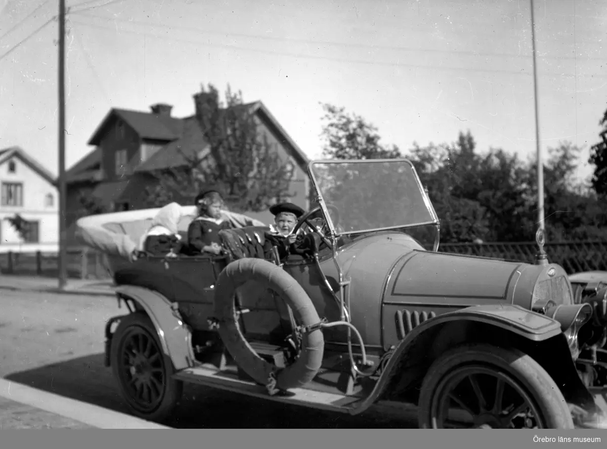 En bil med några personer i. 
Bilen på bilden är av fabrikat Opel från cirka 1912.
Eftersom bilden är tagen av Alfred Thermaenius är det inte så långsökt att tro att bilen skulle kunna tillhöra Gottfrid Thermaenius i Hallsberg. Han ägde nämligen just en Opel, som 1916 registrerades på nummer T10.