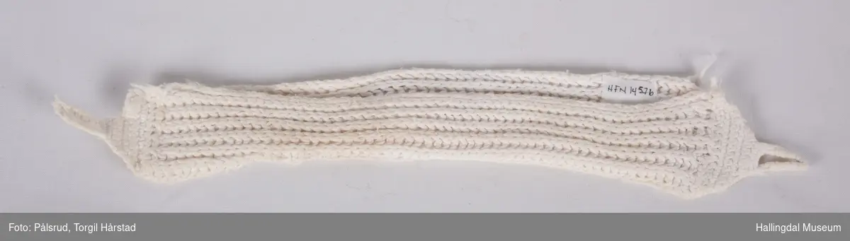 Damebind i hvit patentstrikket bomull med heklete ender. to hemper på hver ende. Formet dobbelt med åpning på den ene siden.