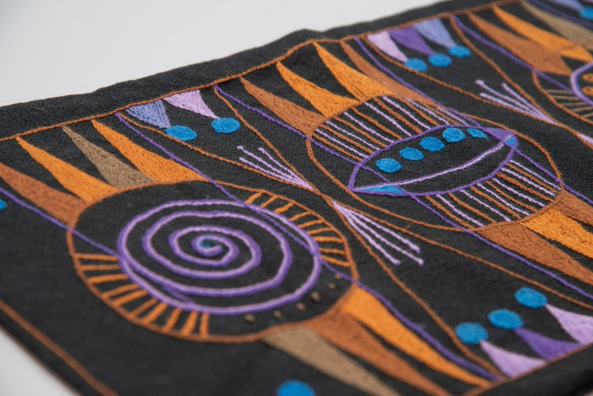 Svart tekstilpose med broderi i oransje, lilla og blå. Geometrisk design. 