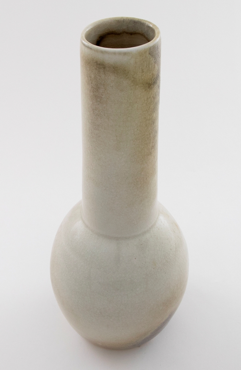 Vase i glasert keramikk. Polykrom glasur i lyse farger. Liten rund kolbe med lang hals.