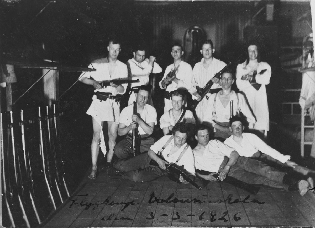Grupporträtt av volontärer på Flygkompaniet på Malmen, 1926. Elva män poserar med gevär på logemente.