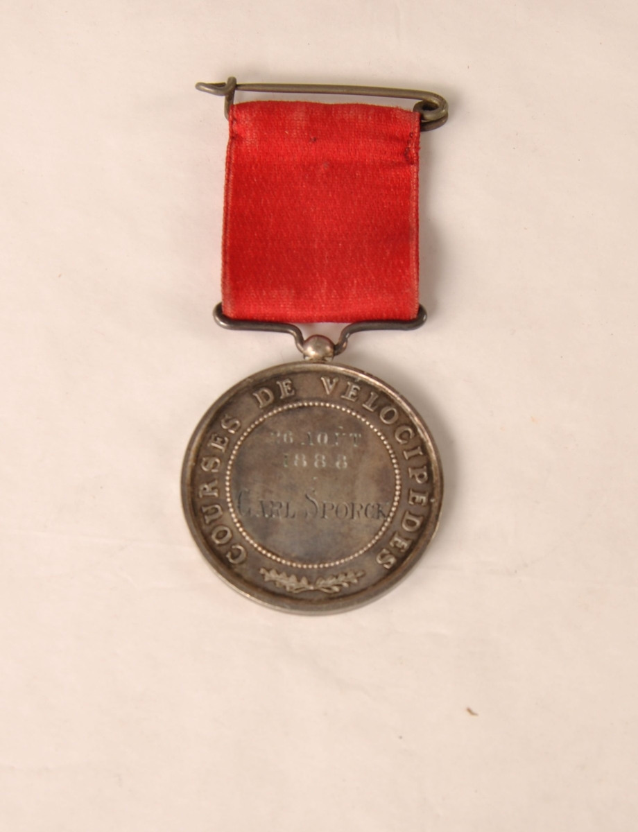 Fransk medalje til Carl Spørck for velosiped-ritt 26. august 1888, Ville de Deauville. I et rødt bånd.