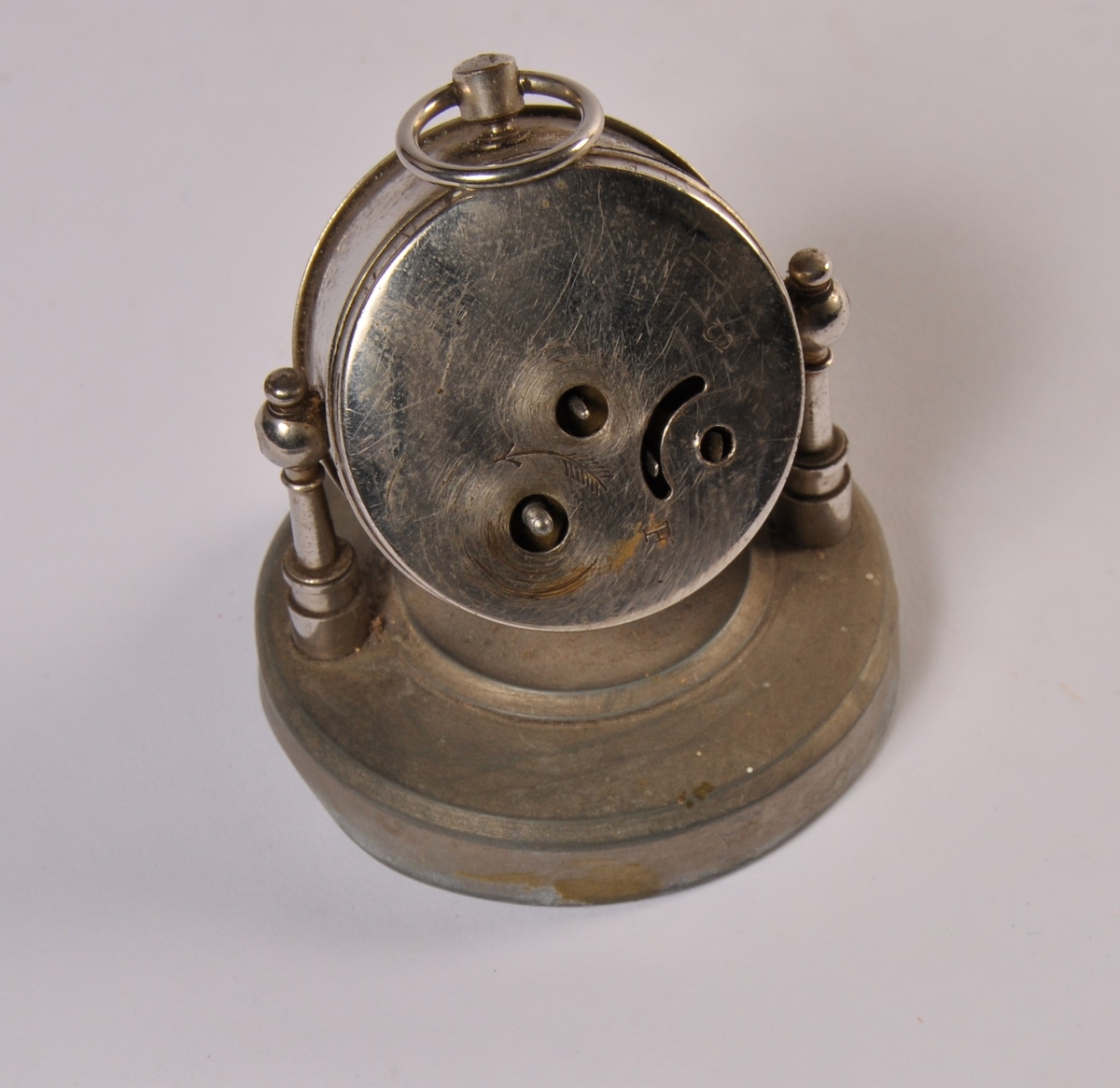 Ur i rund urkasse montert med to metallpinner på tyngre rund fot av metall.
