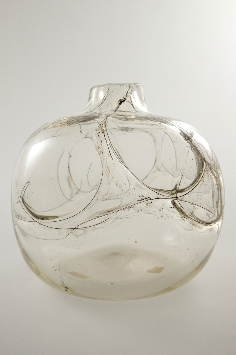 Flattrykket kuleformet vase i klart glass med kort hals. Korpus er dekorert med innlagte ringer av metalltråder på vasens øvre del, og ut ifra disse stråler lange, spisse luftbobler. Puntemerke under vasens bunn.