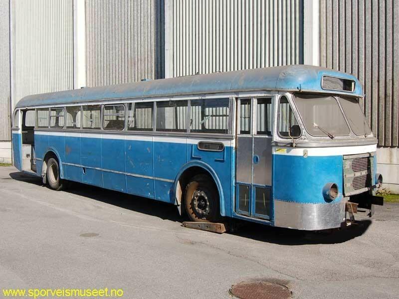Lys blå buss med et hvitt midtskillebånd. Bussen har inngang i front og helt bak. 