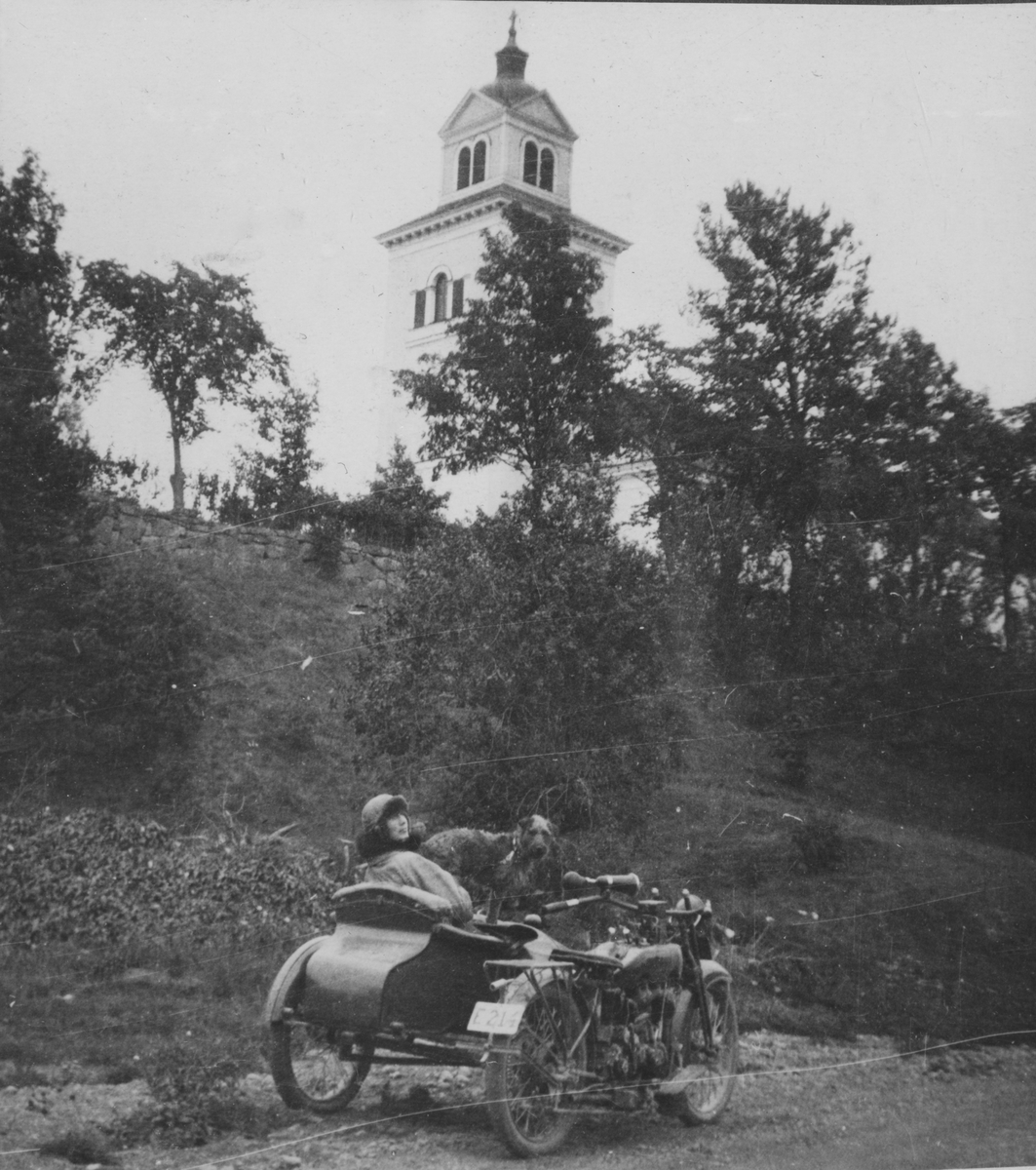 Anna Linderstam och en hund på en motorcykel med sidovagn framför Hammars kyrka, 1925.

Text vid foto: "Hammars kyrka 1925. Bessan. Annika."