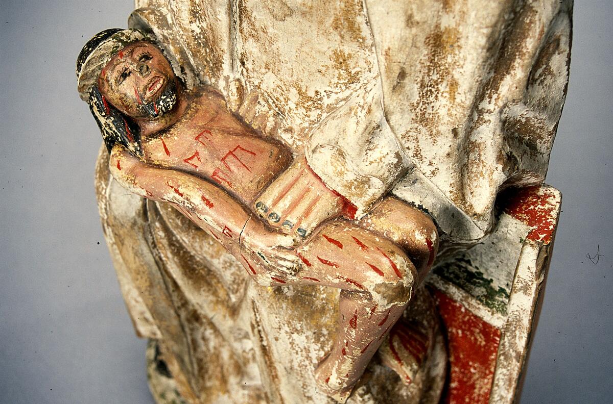 Pietà, Marie klagan. (Maria sörjande den döde Kristus, som är lagd öfver hennes knä). Träskulptur. Maria sittande å bänk med Kristus i liggande ställning i knät.(Marias huvud ovanligt litet i förhållande till kroppen i ö.) Marias dräkt i guld liksom den från huvudet nedhängande manteln. Kristi kropp heltäckt med sår, kring huvudet vriden törnkrona. H.47 cm. Omkr. 1525.  \"Pietà. 1520- eller 30-talet. Denna bild har rätt stor liket med altarskåpsfigurerna i Junsele. Torde vara utförda af någon provinskonstnär. H. 46 cm. Maria sitter på en enkel stol och håller den från korset nedtagne Kristus i sitt knä. Maria är klädd i en lång klänning och mantel. Klänningen är rakt avslutad vid halsen. Klänningens ursprungliga färger har varit guld på utsidan och röd på insidan. Den röda färgen syns vid klänningens kanter, både vid ärmarna och fötterna. Manteln täcker Marias huvud, faller ner på axlarna och sveper om kroppen ända ner till fötterna. Manteln har varit guldmålad på utsidan och blå på insidan. Några fallande veck uppstår vid Marias knä där hon särar på benen för att kunna hålla Kristus kropp. Marias fötter är klädda i svarta skor. Maria håller sin högra hand under Kristus huvud och nacke, den vänstra vid hans midja. Händerna är gråa med röda konturlinjer mellan fingrarna. Naglarna är svarta. Marias ansikte har en hög panna, en stor näsa, ett par halvslutna ögon och en rakt formad tunn mun. Ansiktets målning är fortfarande kvar. Ansiktet är inramat med en svart konturlinje. Ansiktets rosiga kinder kontrasterar mot den ljusgrå huden. De halvslutna ögonen har svarta ögonpupiller. Ögonen och även ögonfransarna är målade med svarta linjer. Munnen är målad med ett rött streck över den tunna överläppen. Marias ansikte är fullt av sorg och betänksamhet.; Kristusfiguren är alldeles naken. Han ligger i Marias knä med böjda ben. Hans högra hand ligger på kroppens högra sida, den vänstra är vänd mot Maria. Kristi bröstkorg är enkelt målad med svarta linjer i tjocka penseldrag. Kroppen liksom ansiktet är stänkt med röda bloddroppar på något ljusrosa hy. Ansiktet har ett svart målat skägg runt en halvöppen mun. Munnen är vit med röda tvärlinjer. En rödbrun konturlinje sträcker sig runt läpparna. Kinderna är röda. Näsan är avslagen. Ögonen är öppna med målade svarta pupiller och konturslinjer med ögonfransar. Ögonbrynen är mörkbruna med målade enstaka hårstrån. En törnekrona i grön färg sitter på Kristus svarta hår. Håret är långt och ligger över nacken. Den avlånga halsen är målad med rosa färg.; Maria sitter på en stol som liknar en väggbänk. Stolen är målad med grön färg längst upp och längst ner, röd färg i mitten och guld vid kanterna. Sidostyckena är röda och gula. Marias fötter vilar på en fotbräda, ursprungligen grönmålad. Stil och datering: Pietàbilden blev mycket populär under 1300- och 1400-talen i Europa. Pietà från Sättna är ovanlig i sitt stilistiska utförande. Kroppens utformning och proportioner är felaktiga. Kristus kropp är onaturligt utformad med felböjd höger arm och hand. Hans vänstra hand är felvänd mot Marias kropp. Marias vänstra hand har fyra fingrar lika långa. Hennes hals är avlång och ansiktet för litet i förhållande till huvudet. Marias kropp är också för stor till den lilla Kristuskroppen om den ska föreställa en vuxen människa. Det är möjligt att man vill föreställa Maria med den döde Kristus förvandlad på nytt till ett barn. En sådan pietàframställning har funnits på medeltiden. Att så är fallet understryks av Kristus nakna kropp.; Skulpturen är ganska ovanlig på grund av dessa naiva drag. Men det finns en hel del andra skulpturer i Norrland som har samma stilistiska drag som denna pietà från Sättna. TEKNISK BESKRIVNING; Baserad på okulär beskrivning. Pigmenten är identifierade genom jämförelse med uppstrykningar av kända pigment. Bindemedel är identifierade med löslighetstest. Träslagen är identifierade genom jämförelse med en provsamling kända träslag. 2002LK. Dimensioner:; Höjd: 47,5 cm; Bredd: 25 cm; Djup: 12 cm; ; Pietàskulpturen är utformad som halvskulptur  och skuren i ljust lövträ i ett stycke. Skulpturen har en grund V-formad urholkning på baksidan (höjd:30 cm och djup: 5 cm). Skulpturen har spår av ett rakt eggverktyg på baksidan (bredd: 6 cm) och en avsågad tapp på hjässan (diameter: 1,2 cm). På skulpturens baksida finns en stor järnspik. Skulpturens framsida är grunderad med animaliskt lim och krita. På några ställen är ojämnheter i underlaget utjämnade med linneväv. Karnationen på Maria och Kristus är rosa och tonad mörkare vid hårfäste, ögonlock, halslinning m.m. Iris, pupiller och naglar är svarta. Kristus hår har ristningar i grunderingen och är målad med brunt, törnekrona är målad med kopparresinat. Blodflödet på Kristus är målad med cinnober. Utsidorna på Marias mantel och tunika är förgylld med polerat bladguld. Mantelns insida är målad i azurit i limfärg på svart undermålning. Tunikans insida är röd. Marias skor är svarta. Tronen är förgylld med polerat bladguld och bemålad med cinnober och kopparresinat. Tronens utsida har orange bemålning. Marksockeln är målad med kopparresinat. Från Sättna k:a Medelpad 1912
