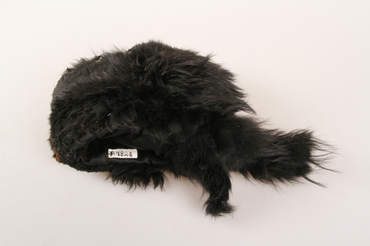 Muffe i svart pelsverk, med tillaget hode med falsk nese og øyne, samt hale. 