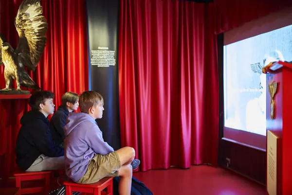 Tre gutter, elever, sitter å ser på en film i Jugendabteilung.