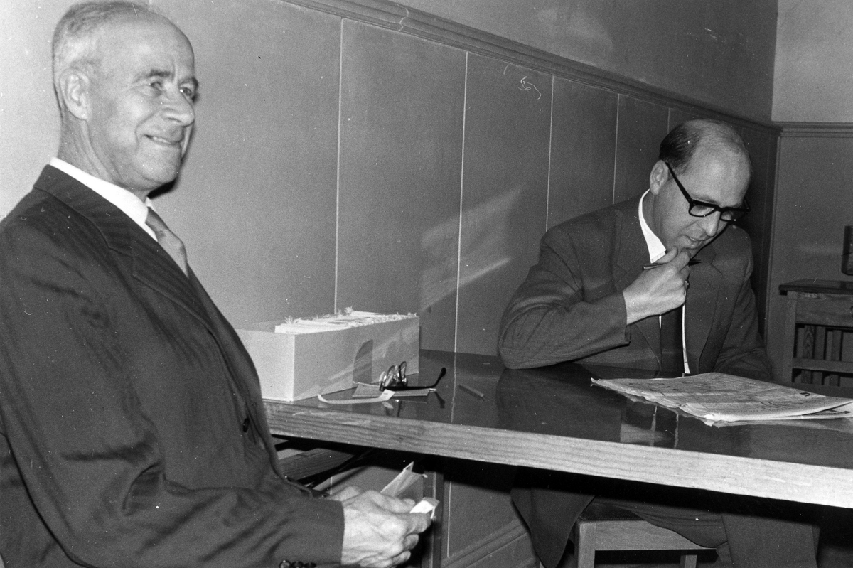 Bild på två män, de sitter vid ett bord där mannen längst från kameran läser ur en tidning.
Kyrkofullmäktigeval 21 oktober 1962.