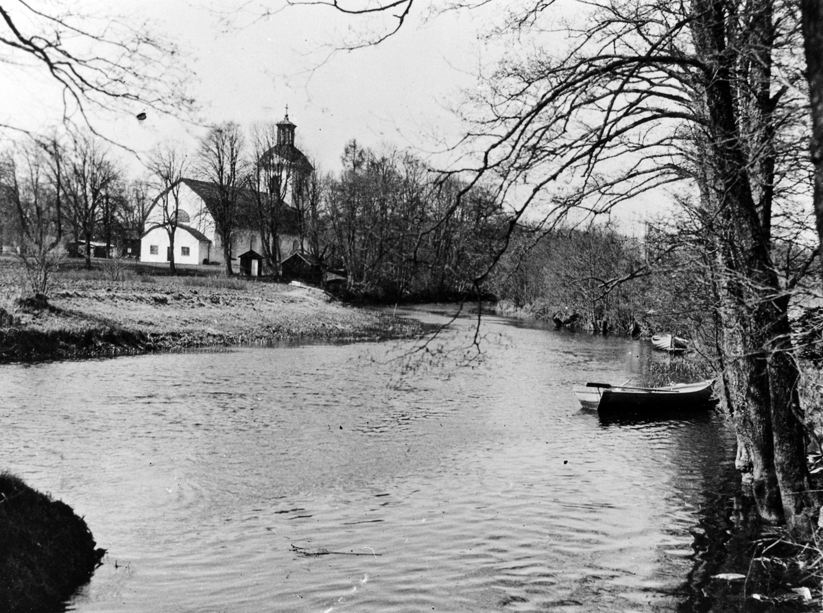 Landskyrkan i Alingsås från andra sidan Säveån, roddbåtar ligger förtöjd vid strandkanten.
Foto mot väster.