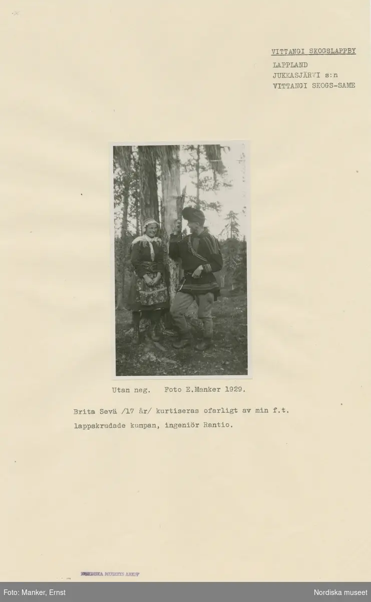 Brita Sevä, 17 år, och ingenjör Rantio står vid ett träd i Tuolpukka, Jukkasjärvi socken, och samtalar. Båda är iklädda samisk dräkt.