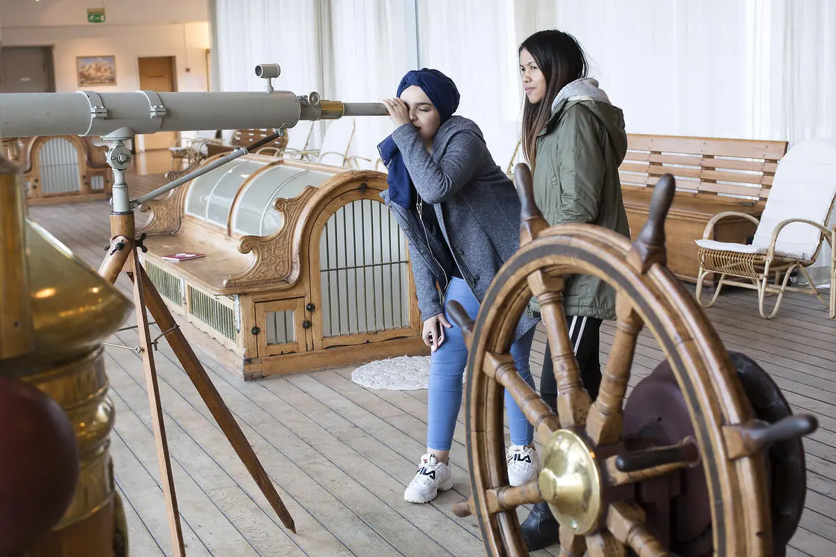 To damer bruker kikkerten på promenadedekket i andre etasje på museet