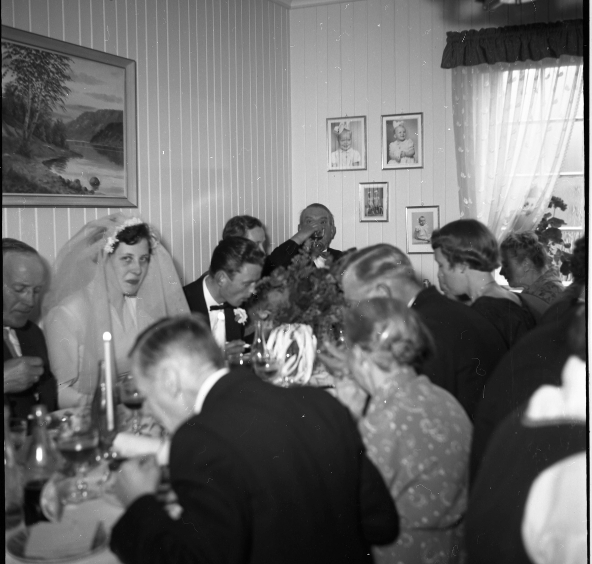 Bilde av penkledde gjester sittende til bords. Bryllupsfest. Bruden kan sees til venstre i bildet.