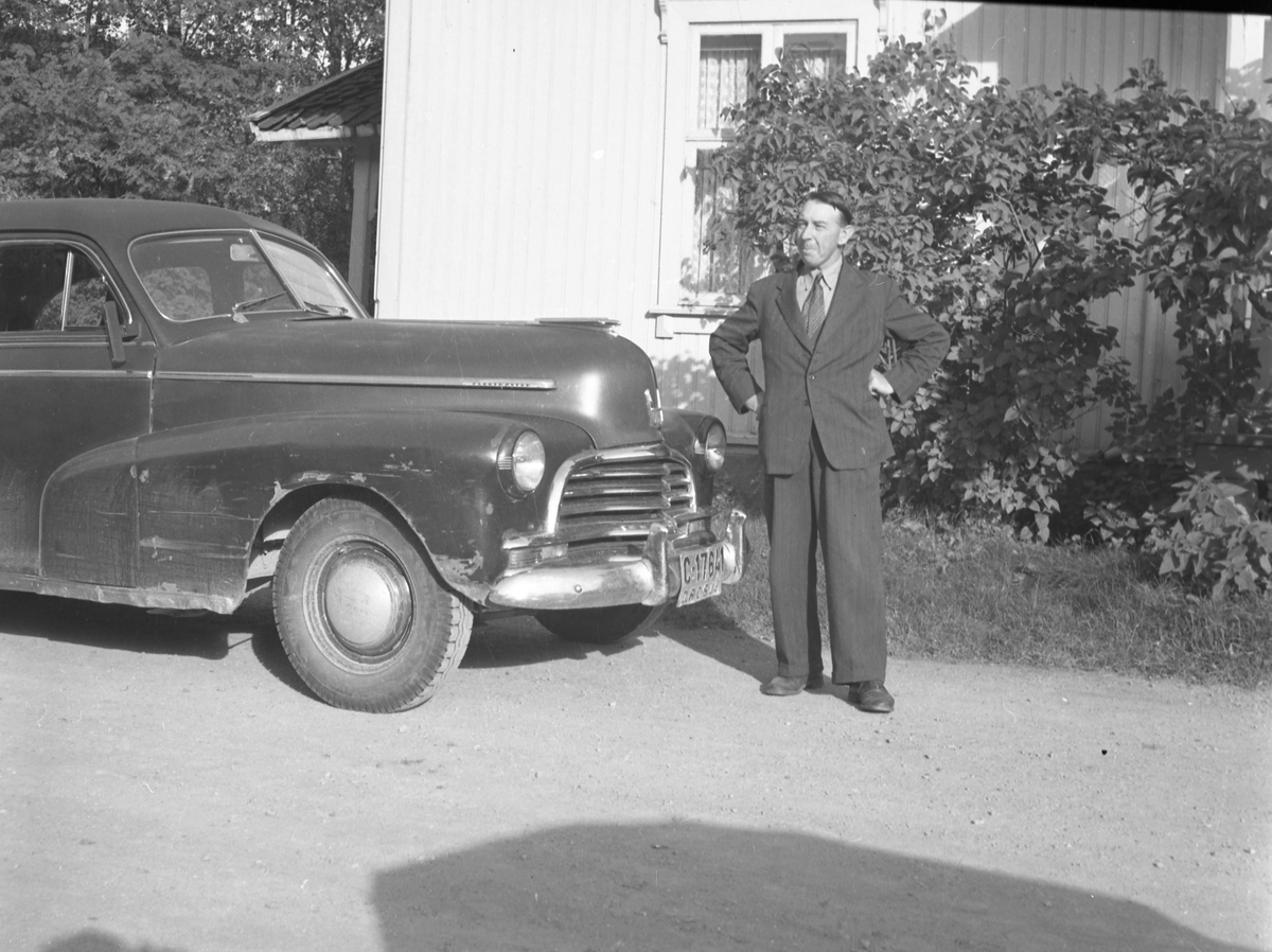 En mann i dress stående foran en drosje med skiltnummer C17641.