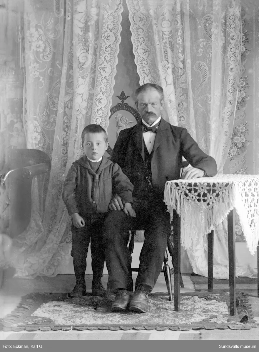 Porträttbild i hemmiljö med en man och en pojke, Indal. Ur Karl Eckmans samling.