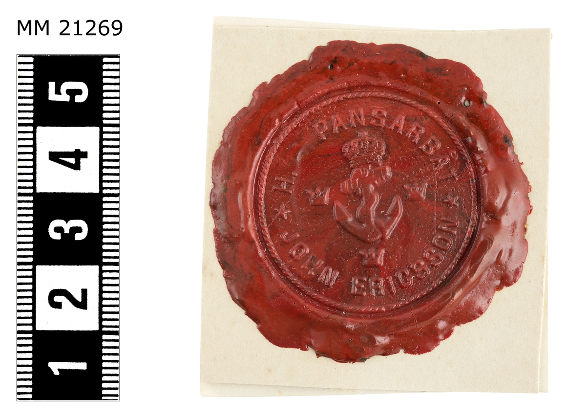 Sigillavtryck av rött lack på papper. I mitten krönt stockankare omgivet av tre kronor. Längs kanten text: "H.M. pansarbåt John Ericsson".